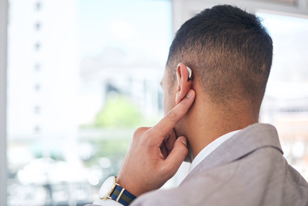 Man pointing to his behind-the-ear hearing aid.