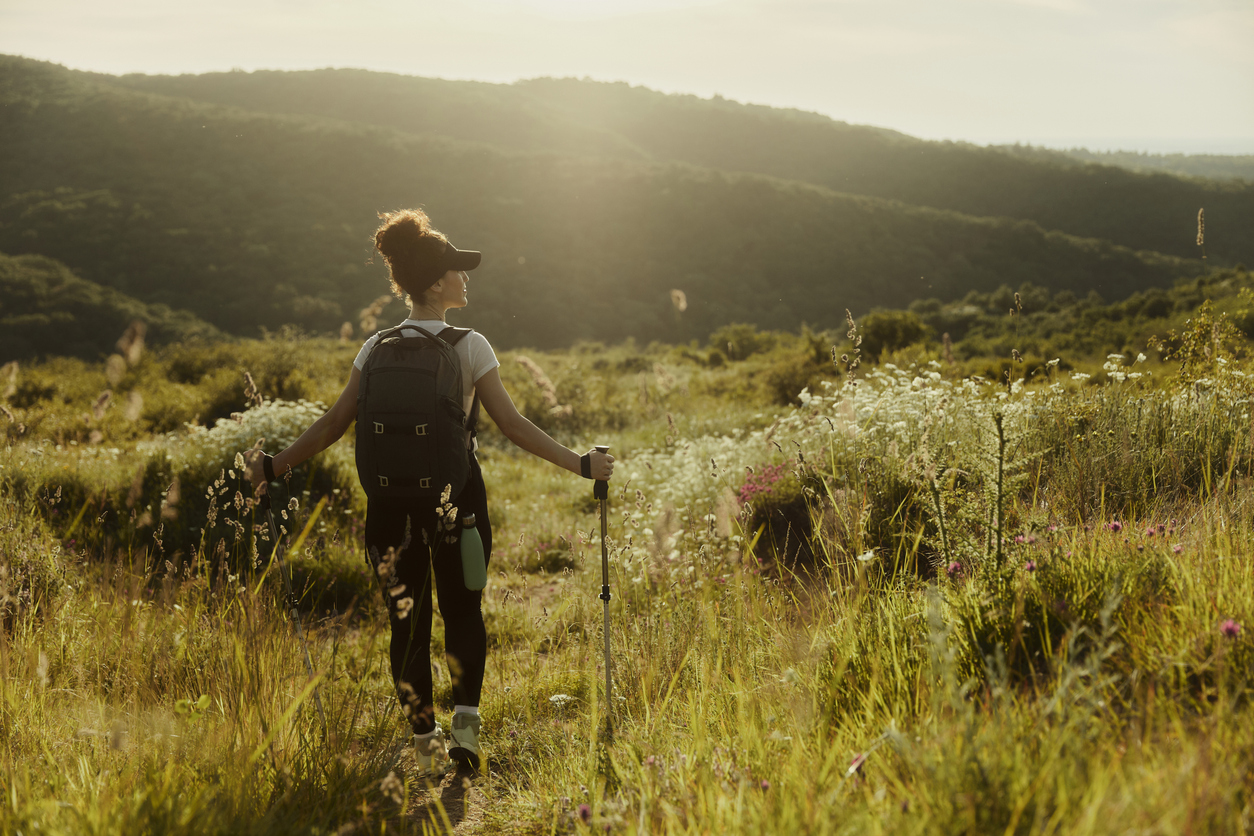 Woman hiking in a grassy meadow at golden hour.