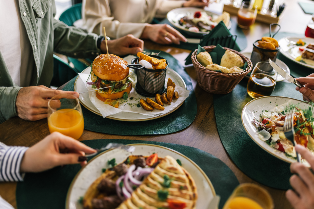 Group of happy friends eating lunch together in a restaurant. They eat delicious salads, hamburgers, bread and meat.