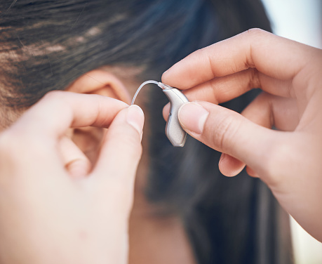 Close-up hands showing a patient how to install a hearing aid.